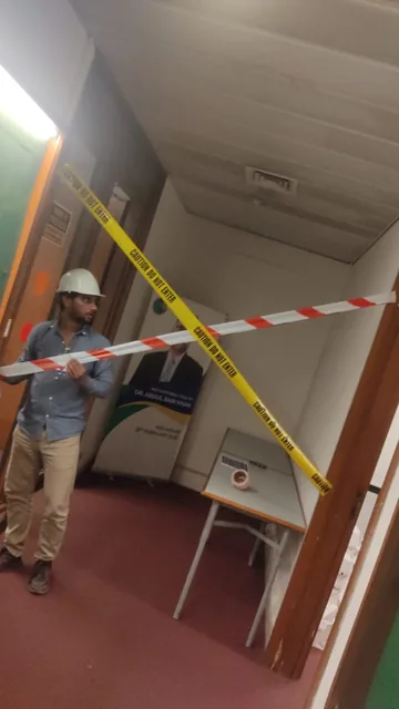 Worker beside red-and-white and yellow barrier tape across an interior doorway.