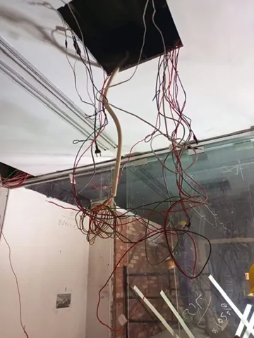 Bundle of loose electrical cables hanging from an open ceiling panel above a glass partition.