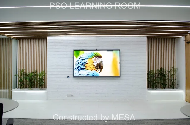 Wall-mounted screen displaying a colourful bird between timber-toned slat panels and white planters, with original project and MESA overlays.