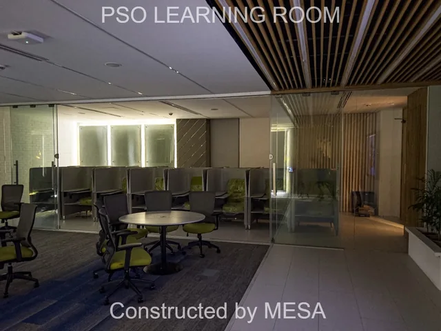 Learning room in lower light with round tables, individual seats behind glass, timber-toned ceiling slats and original project and MESA overlays.
