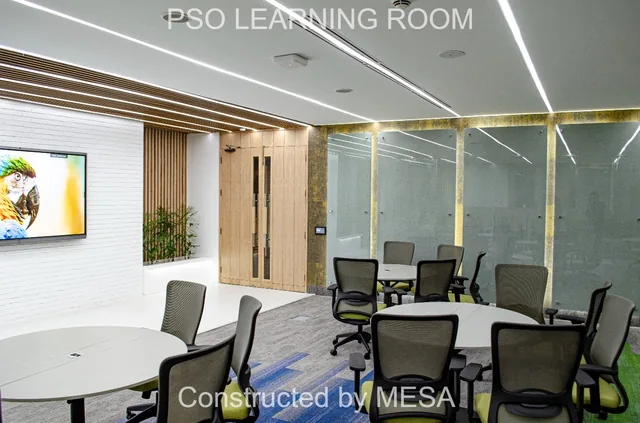 Round tables and chairs facing timber-toned doors beside a wall display, white planter and illuminated vertical wall panels, with original overlays.
