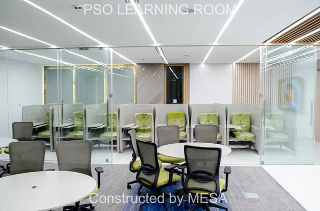 Round table and mesh-backed chairs in front of glass-enclosed individual seats with lime-green cushions, some still wrapped, retaining original overlays.