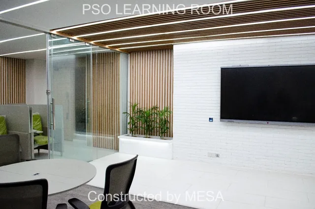 Dark wall-mounted screen on a white brick-textured wall beside a planted trough, vertical slats and clear glazing, with original overlays.