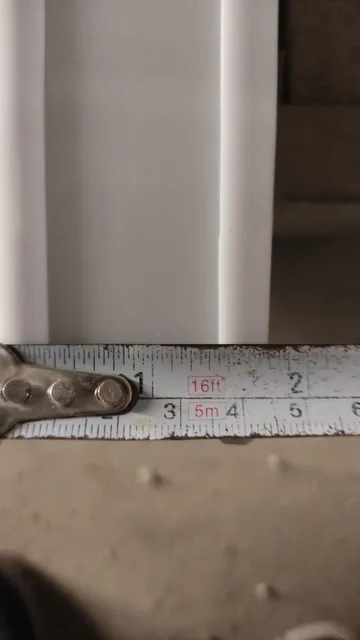 Close-up of a pale profiled section with a metal measuring tape held across its width.