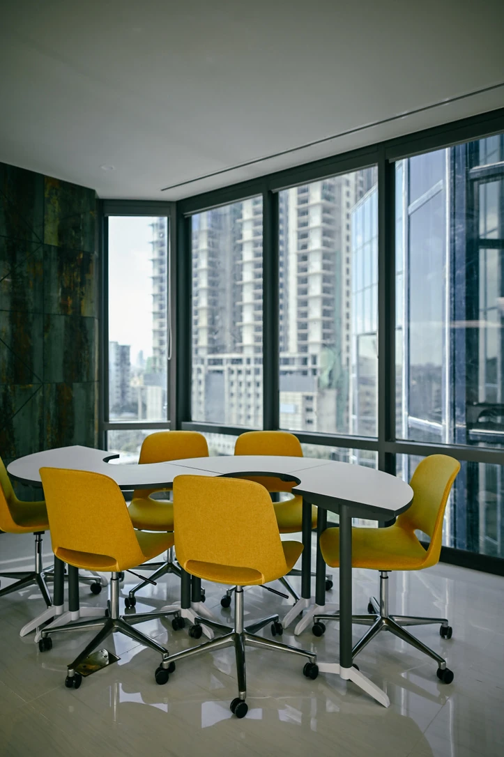 PSO 6th & 7th: Yellow chairs around a table beside corner glazing. 6th–7th-floor interior photography.