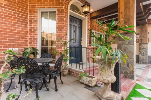 Brick entrance porch with navy door, arched fanlight, black metal garden table and chairs, potted plants and lantern.