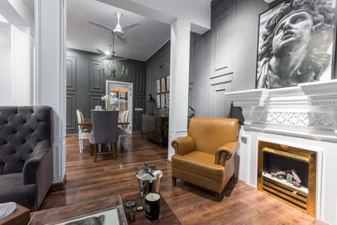 Sitting room with white fireplace, mustard armchair and gray panelling, opening toward a dining room beyond.
