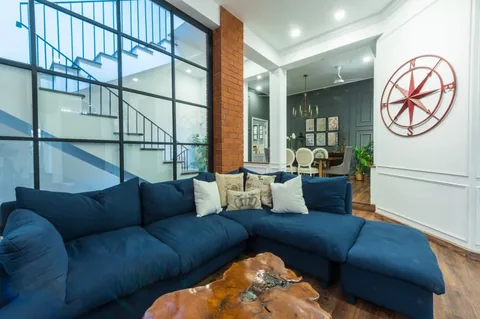 Deep blue corner sofa and live-edge coffee table beside a black-framed glazed staircase wall, with a view through to the dining area.