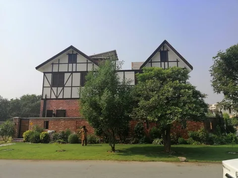 Broad daytime street view of paired gables, pale upper walls, dark linear details, brick boundary and green lawn with trees.