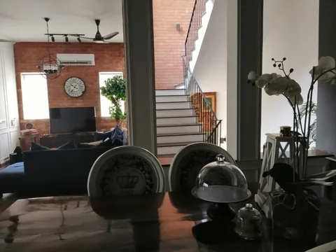 View across a dining table and chairs toward the blue sofa, bright windows and staircase with a brick wall.
