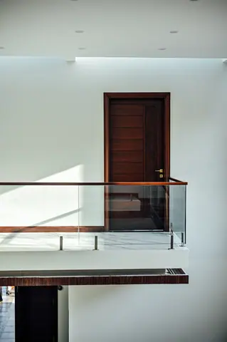 Dark timber door across a double-height opening with a glass balustrade and white walls.