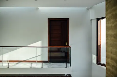 Sunlight on a white upper landing with a timber door, glass railing and side window.