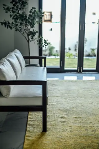 Pale sofa with a dark timber frame beside a green rug, potted tree and tall glazed garden doors.