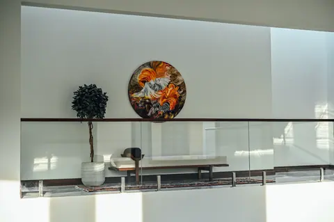 Wide view of a bench, patterned rug, tree and circular artwork behind a glass gallery balustrade.