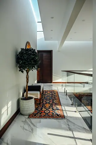 Potted tree, bench and patterned runner beneath a narrow skylight beside a glass gallery rail.