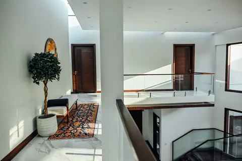 Wide view across a white atrium with glass balustrades, timber doors and a planted gallery corner.