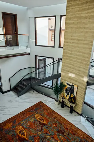 High view into an entrance hall with a tall stone wall, open stair, artwork and patterned rug.