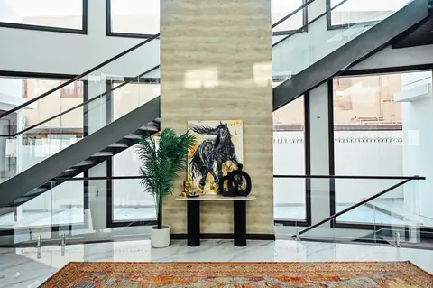 Console with artwork and plants against a pale stone wall beneath crossing stair flights.