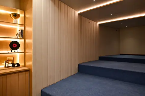 Tiered blue-carpeted platforms beside vertical wall panels, warm ceiling light strips and display shelves.