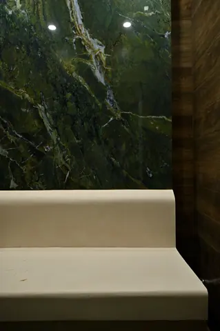 White curved bench against a dark green wall with pronounced pale stone veining.
