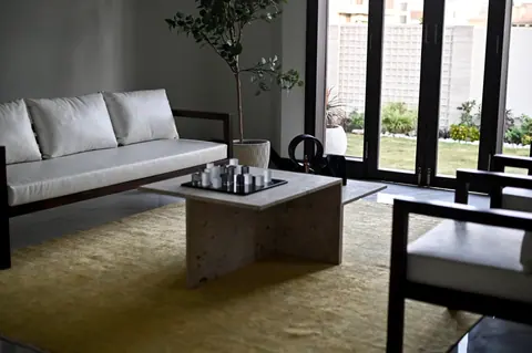 Pale sofa and timber armchairs around a stone table beside tall garden doors.