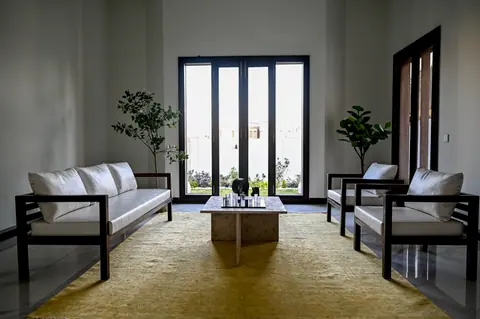Wide view of a sitting room with pale sofa and armchairs, stone table and tall garden doors.