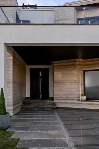 Entrance steps and patterned paving leading to a shaded doorway within a pale stone-clad porch.