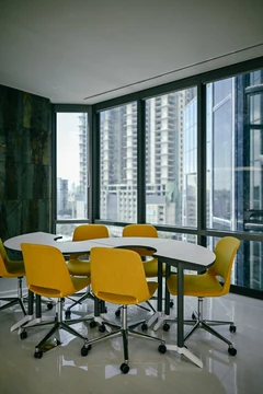 PSO 6th & 7th: Yellow chairs around a table beside corner glazing. 6th–7th-floor interior photography.